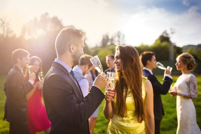 Wedding guests clinking glasses while the newlyweds drinking champagne in the background