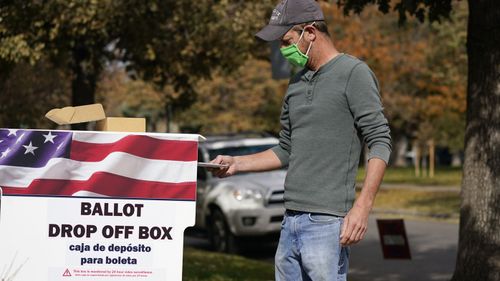 A voter wears a face covering as he place a ballot in a drop box outside the La Familia Recreation Center, south of Denver.