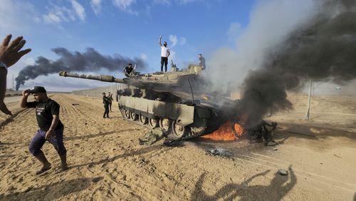 Palestinians celebrate by a destroyed Israeli tank at the Gaza Strip fence east of Khan Younis on Saturday, Oct. 7, 2023. 