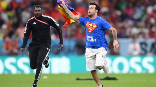 A pitch invader holding a rainbow flag and political messages about Ukraine invades the field during Portugal's match with Uruguay.