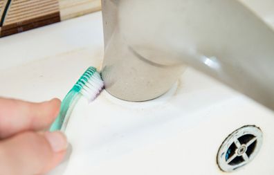 Close up view of woman hand cleaning bathroom sink with toothbrush. Home cleaning hack, fits small spaces to clean off mould and dirt.