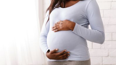 Black woman enjoying her pregnancy, hugging her tummy next to window at home, cropped, panorama with copy space