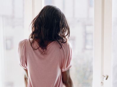 Young woman looking out window sadly