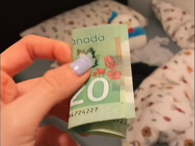 Mum holding money in front of a messy room.