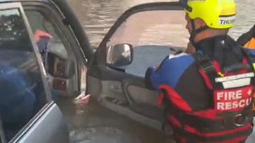 A firefighter rescues a man trapped in a flooded four-wheel drive.