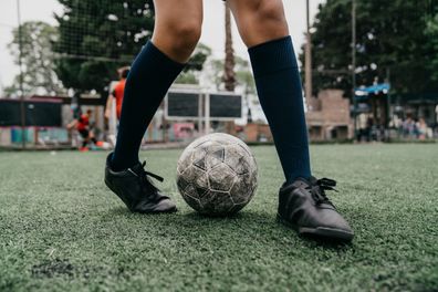 Detail of foot dribbling with soccer ball. Selective focus. Kids playing soccer in the background. Black soccer shoes.