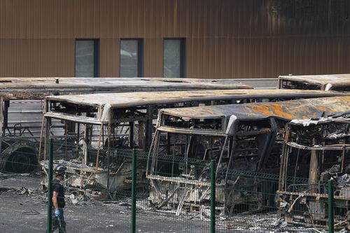 A police investigator watches charred buses on a third night of unrest, Friday, June 30, 2023 at the bus depot of Aubervilliers, outside Paris. 