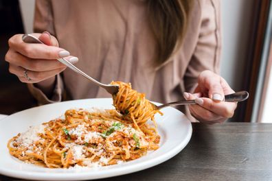 girl eats Italian pasta with tomato, meat. Close-up spaghetti Bolognese wind it around a fork with a spoon. Parmesan cheese.