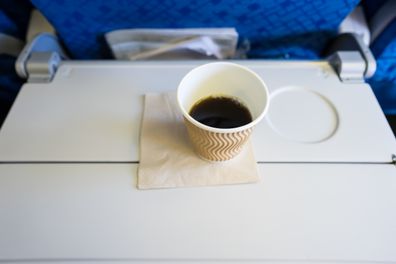 a cup of coffee and a piece of paper on the foldable table on the airplane