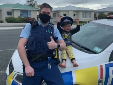 New Zealand Police Officer with a four-year-old boy posing for a photo on patrol car. 