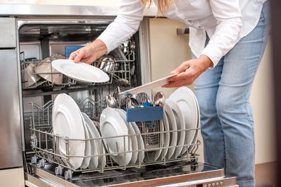 Adult Woman Unloading Dishwasher In The Kitchen