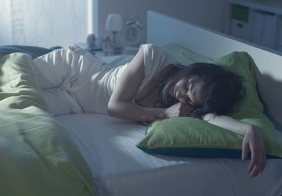 Young woman sleeping in bed at night and lying on her arms