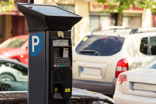 Parcometro con pannello solare per il consumo di energia alternativa accanto ad un paio di auto in un parcheggio