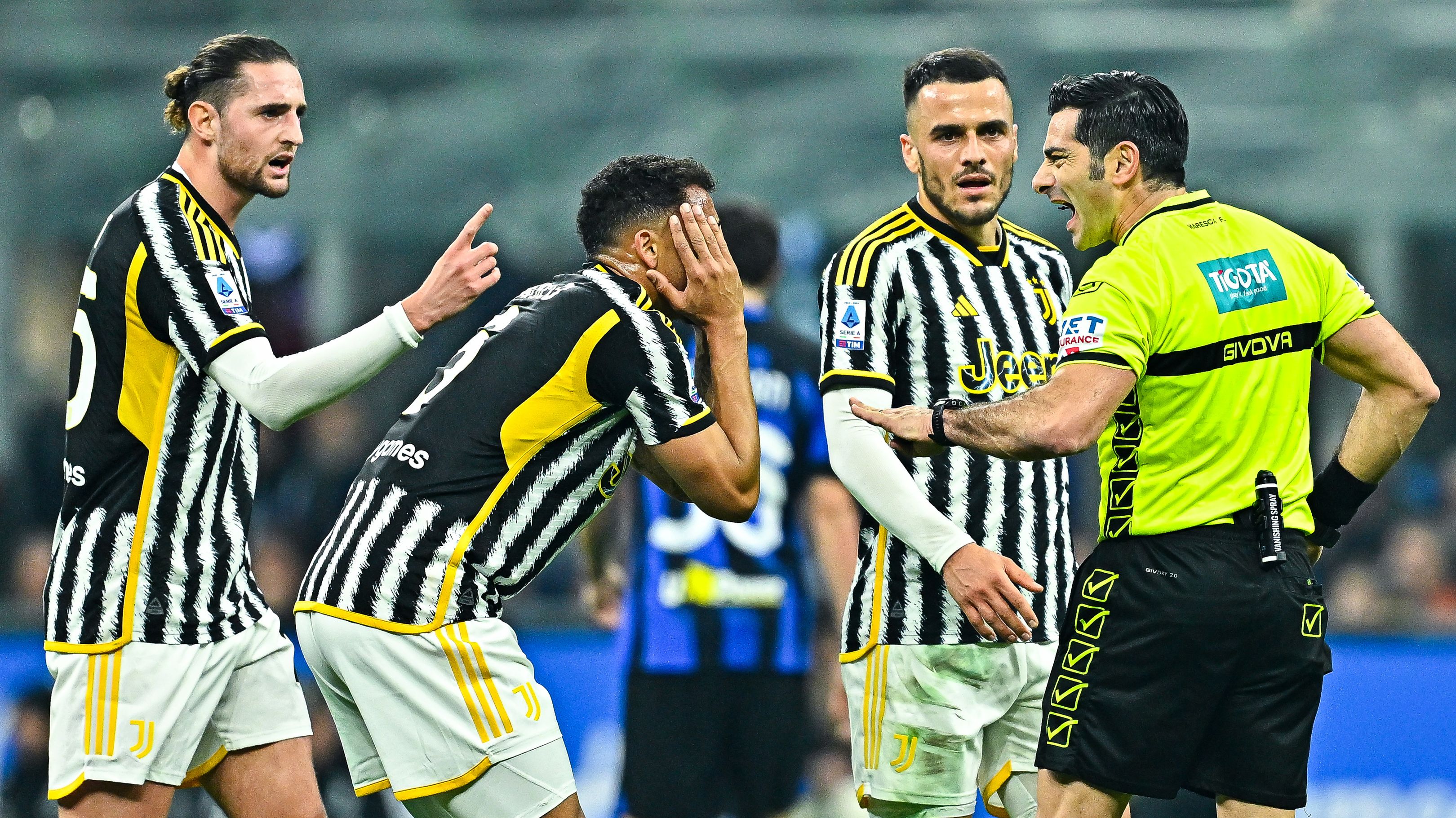 Luiz Danilo of Juventus (second from left) complains with referee Fabio Maresca after being shown a yellow card during the Serie A match between FC Internazionale and Juventus.
