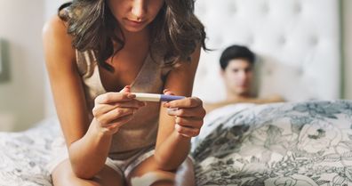 Shot of a woman taking a pregnancy test at home with her boyfriend lying in the background