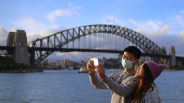 People wear face masks in front of the Sydney Harbour Bridge in Sydney, Monday, March 9, 2020.