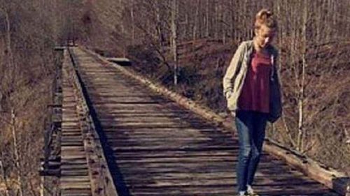 Une photo prise d'Abigail marchant sur un pont ferroviaire abandonné avec une silhouette sombre considérée comme le tueur au loin.