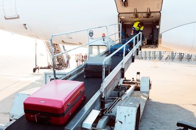 Exterior shot of a young man taking luggage off the plane. Airport ground crew at work.