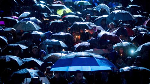 People stand under umbrellas as rain falls during a candlelight vigil to honour the victims of the Paris terrorist attacks, in Vancouver, B.C. (AAP)