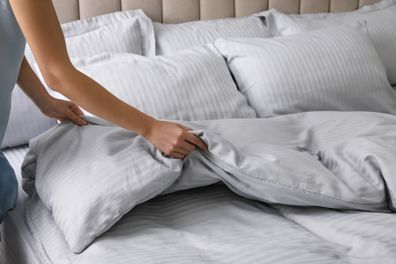 Woman putting soft blanket on bed with pillows, closeup