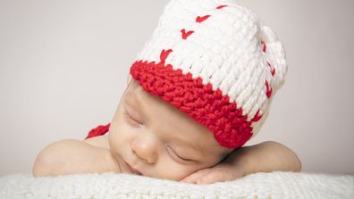 A sleeping 2.5 month old baby boy wearing a baseball hat.