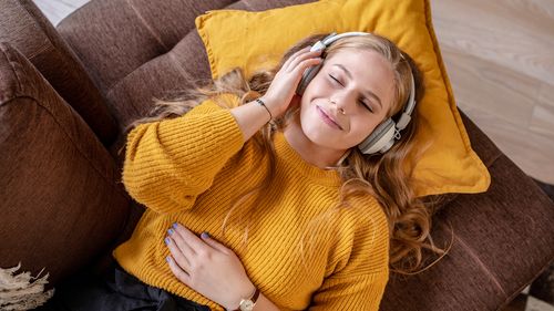 Young woman with headphones laying on the couch and smiling listening to music