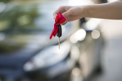 Arm holding keys to new car. New car with bow.