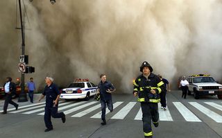 Eerste hulpverleners op de vlucht voor een stofwolk na de ineenstorting van het World Trade Centre. (AFP)