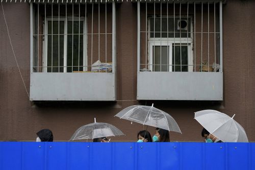 Residents holding umbrellas line up in the rain along the barricaded fence for COVID tests outside the locked-down apartment building in Beijing.