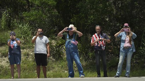 People watch as President Donald Trump and first lady Melania Trump pass in a motorcade in Kerrville, Texas, to monitor flood damage, Friday, July 11, 2025. (AP Photo/Jacquelyn Martin)