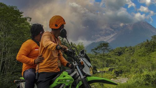 Des hommes regardent le mont Merapi libérer des matériaux volcaniques lors d'une éruption à Sleman, en Indonésie, le samedi 11 mars 2023. 