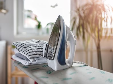 Iron and cloth on ironing board at laundry room with washing machine visible in the background