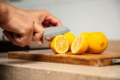 The woman is cutting the yellow lemon with a knife