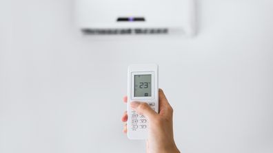 A person holding the remote for an air conditioning unit