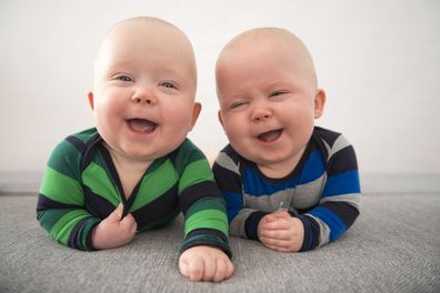 Identical twins lying down on grey mattress