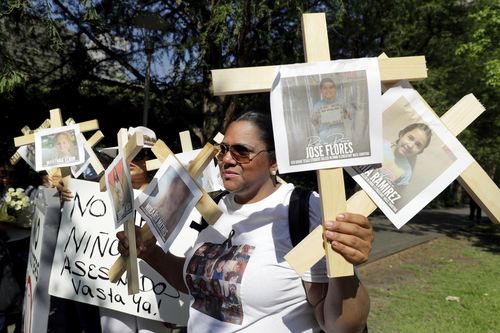 Nancy Pablo, with the Alianza Latina International, holds crosses with photos of victims of the Robb Elementary School shooting as she protests with others at Discovery Green Park across the street from the National Rifle Association Annual Meeting at the George R. Brown Convention Center Friday, May 27, 2022, in Houston. (AP Photo/Michael Wyke)