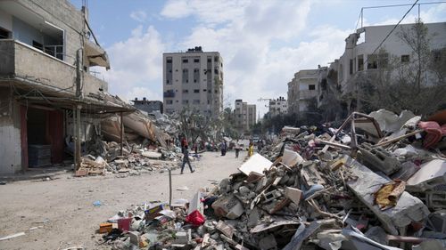 Palestinians walk by buildings destroyed in Israeli airstrikes in Nuseirat camp in the central Gaza Strip.