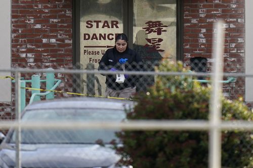 An investigator carries markers outside the crime scene of Star Dance Studio in Monterey Park.