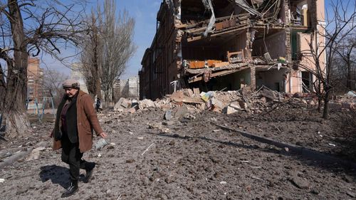 A woman walks past building damaged by shelling in Mariupol