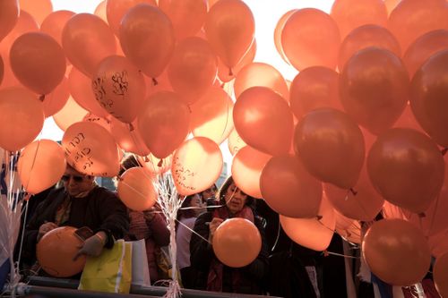 People write on orange balloons during an event to mark the first birthday of Kfir Bibas.