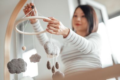 Pregnant woman hanging mobile over cot in nursery