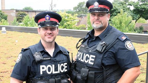 Two police officers have been hailed as heroes after rescuing two people from a flooded lift in Toronto.