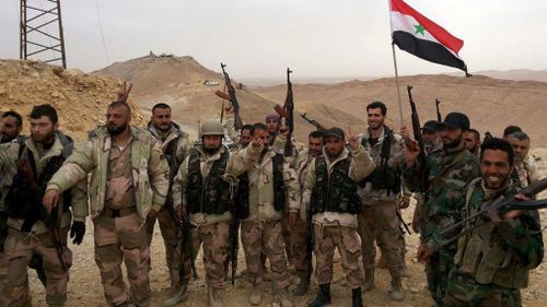 Syrian government soldiers holding the national flag and posing during an operation in Palmyra. (Supplied/ Syrian Arab News Agency)