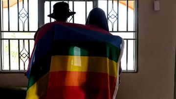 A gay Ugandan couple cover themselves with a pride flag