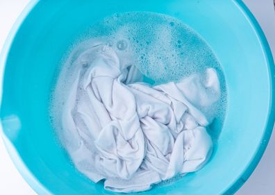 Hand laundry washing clothes in blue plastic basin, soaked white cloth handwash, housework