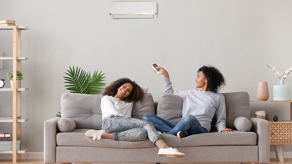 Woman and girl sit on couch above air conditioning. 