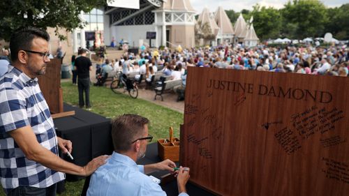Sen. Scott Dibble, DFL - Minneapolis, signs a wooden board as his husband Richard Leyva put his hand on his shoulder during the memorial service for Justine Damond. (AAP)