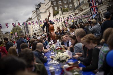 A musician plays his double bass as people sit at long tables to eat their lunch as part of the Big Lunch celebration in London, Sunday, May 7, 2023. The Big Lunch is part of the weekend of celebrations for the Coronation of King Charles III. 