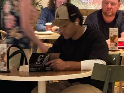 Actor Josh Heuston reading Onyx Storm at Sydney airport