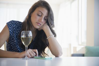 Woman looking at phone with glass of wine